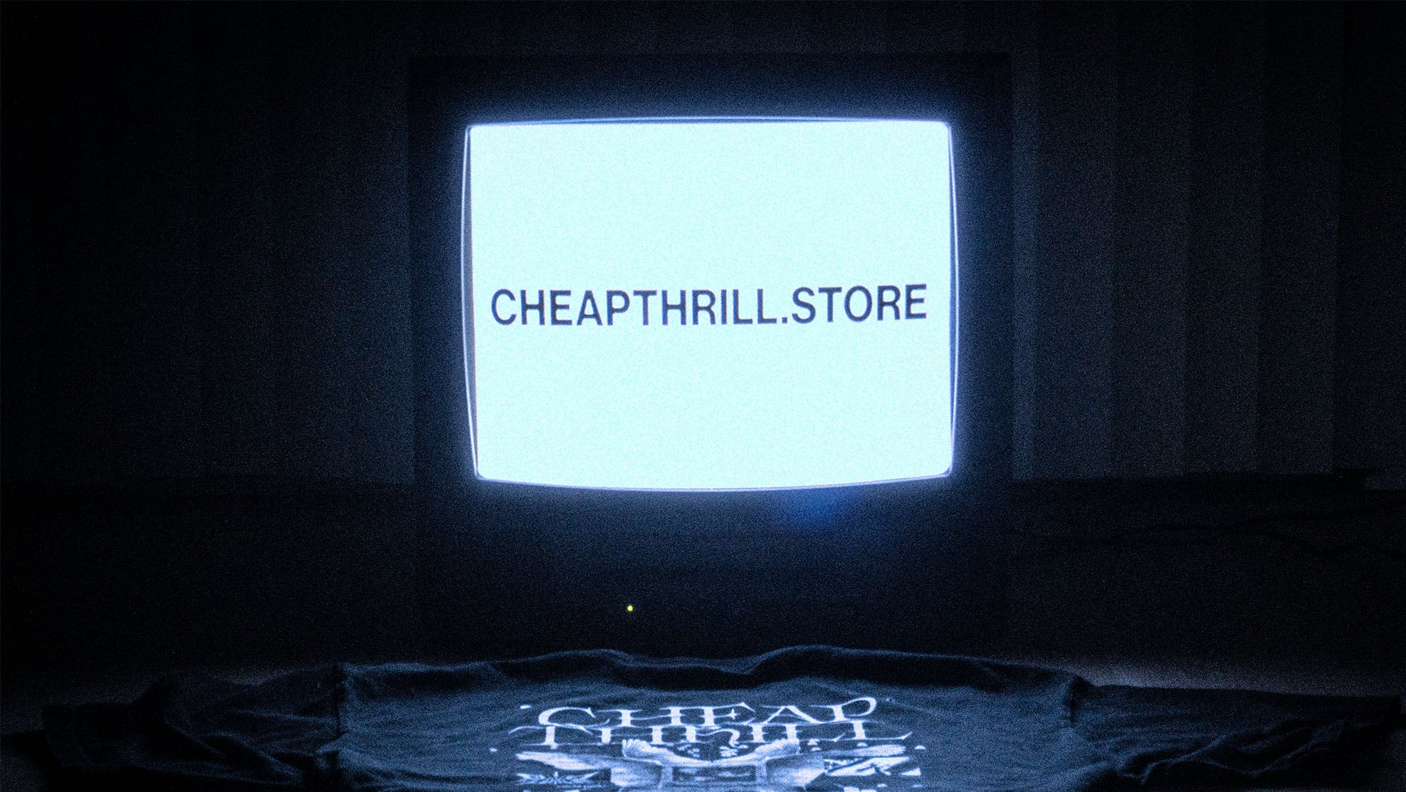 Vintage television set displaying 'CHEAPTHRILL.STORE' with a dark background, with a shirt at the bottom